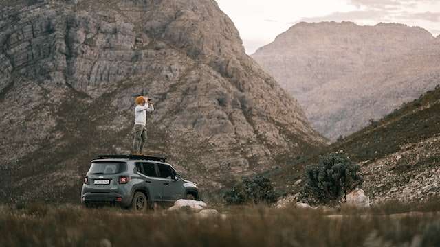 Foto de um homem em frente a uma montanha no teto de um jeep renegade